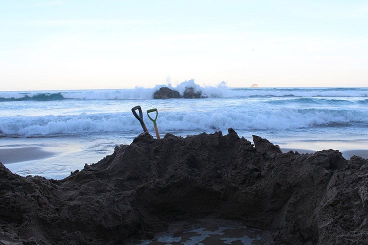 Two spades sticking out of pile of sand on beach